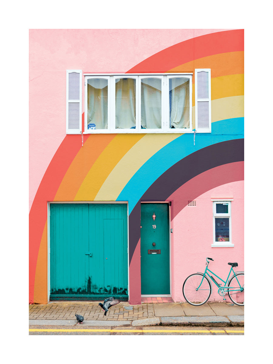 Fotografie eines Hauses mit Regenbogenfarben, grüner Tür und einem Fahrrad, mit zwei Tauben davor.