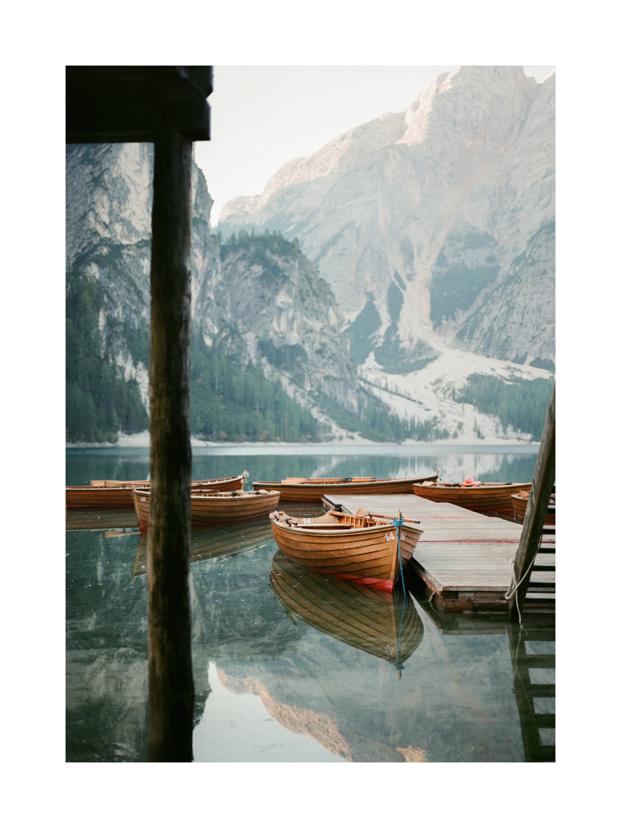 Fotografie von Holzbooten an einem Steg auf einem See mit Bergen im Hintergrund.