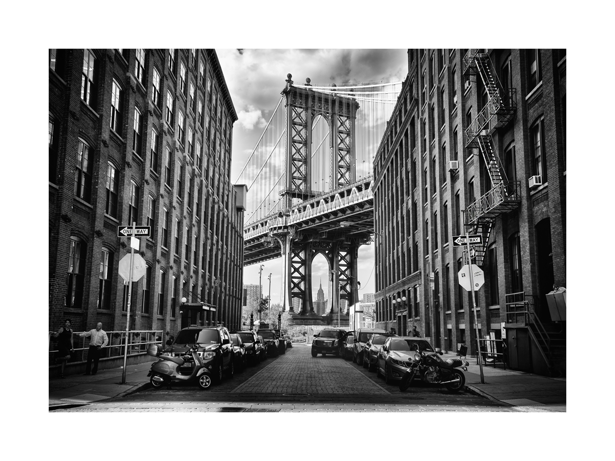 Schwarz-weiß-Fotografie der Manhattan Bridge in New York mit Gebäuden und Autos.
