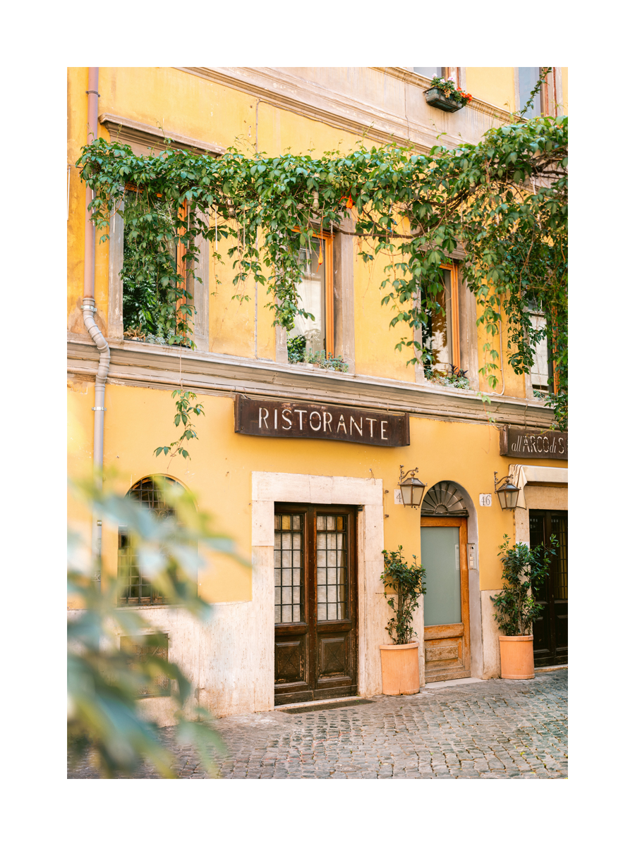 Fotografie eines gelben Restaurants mit grünen Blättern und italienischer Architektur.