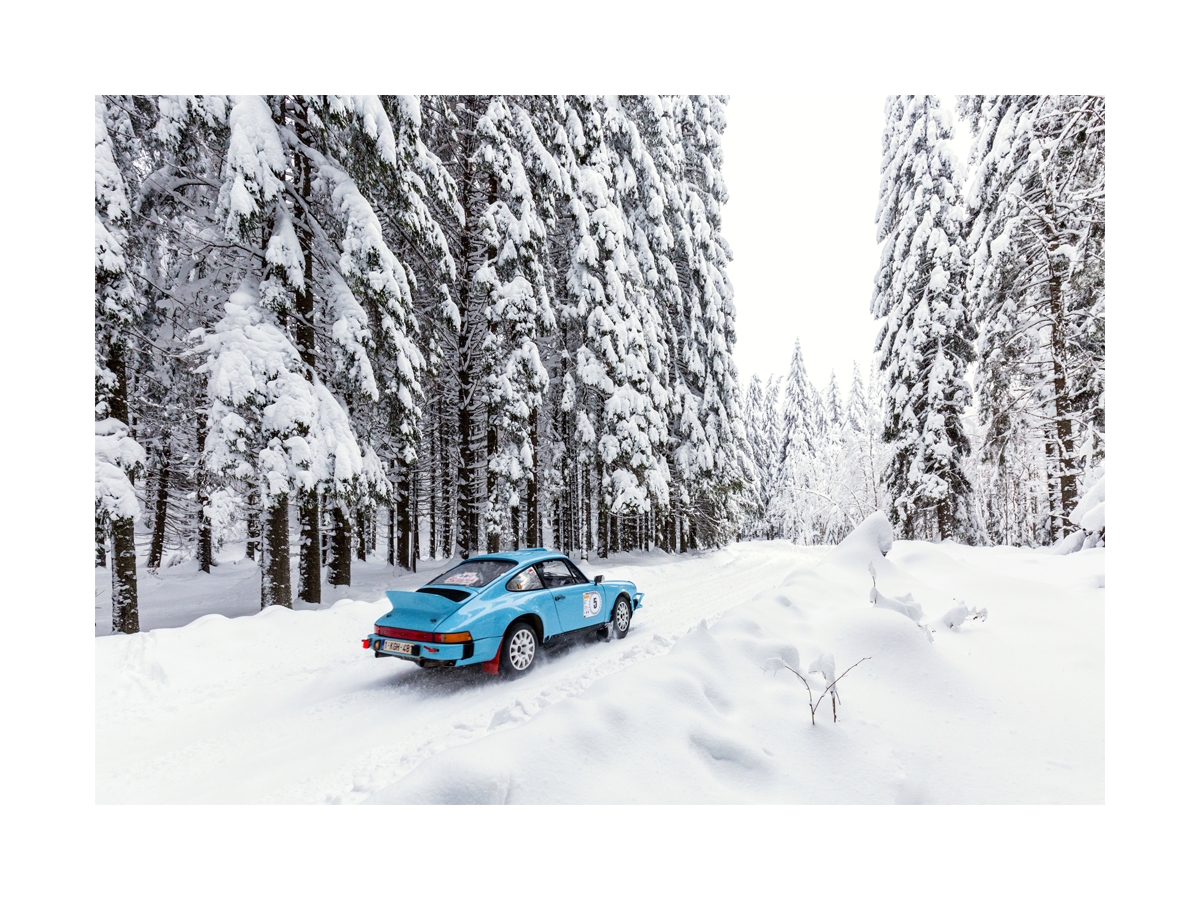 Fotografie eines blauen Autos, das durch einen verschneiten Wald fährt.