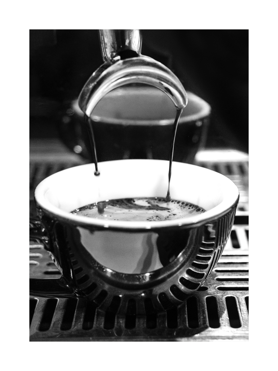 Schwarz-Weiß-Fotografie eines Espressos, der in eine Tasse fließt.