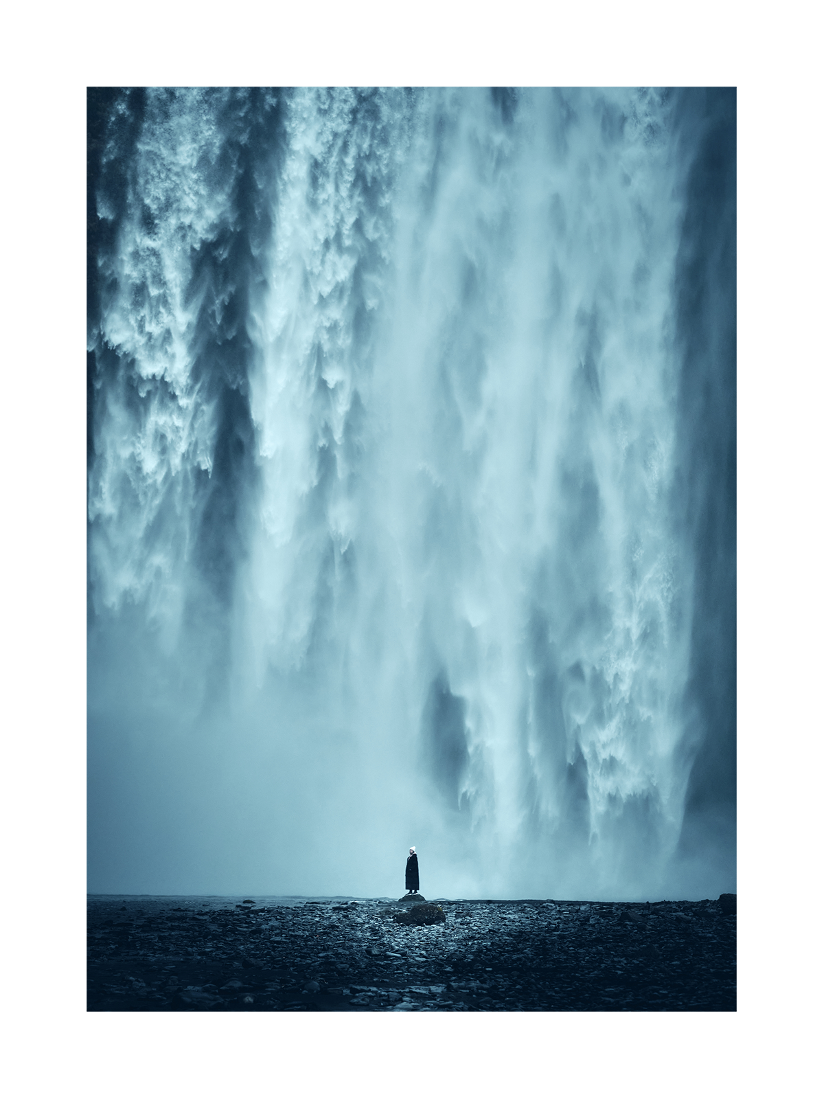 Fotografie eines großen Wasserfalls mit einer Person, die auf einem Felsen steht.