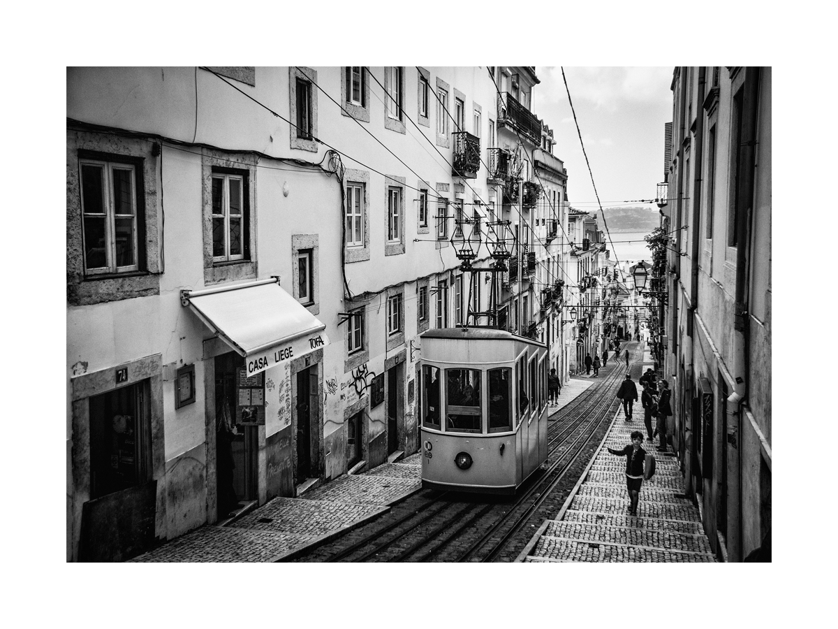 Schwarz-weiß-Fotografie einer Straßenbahn in einer Straße in Lissabon.