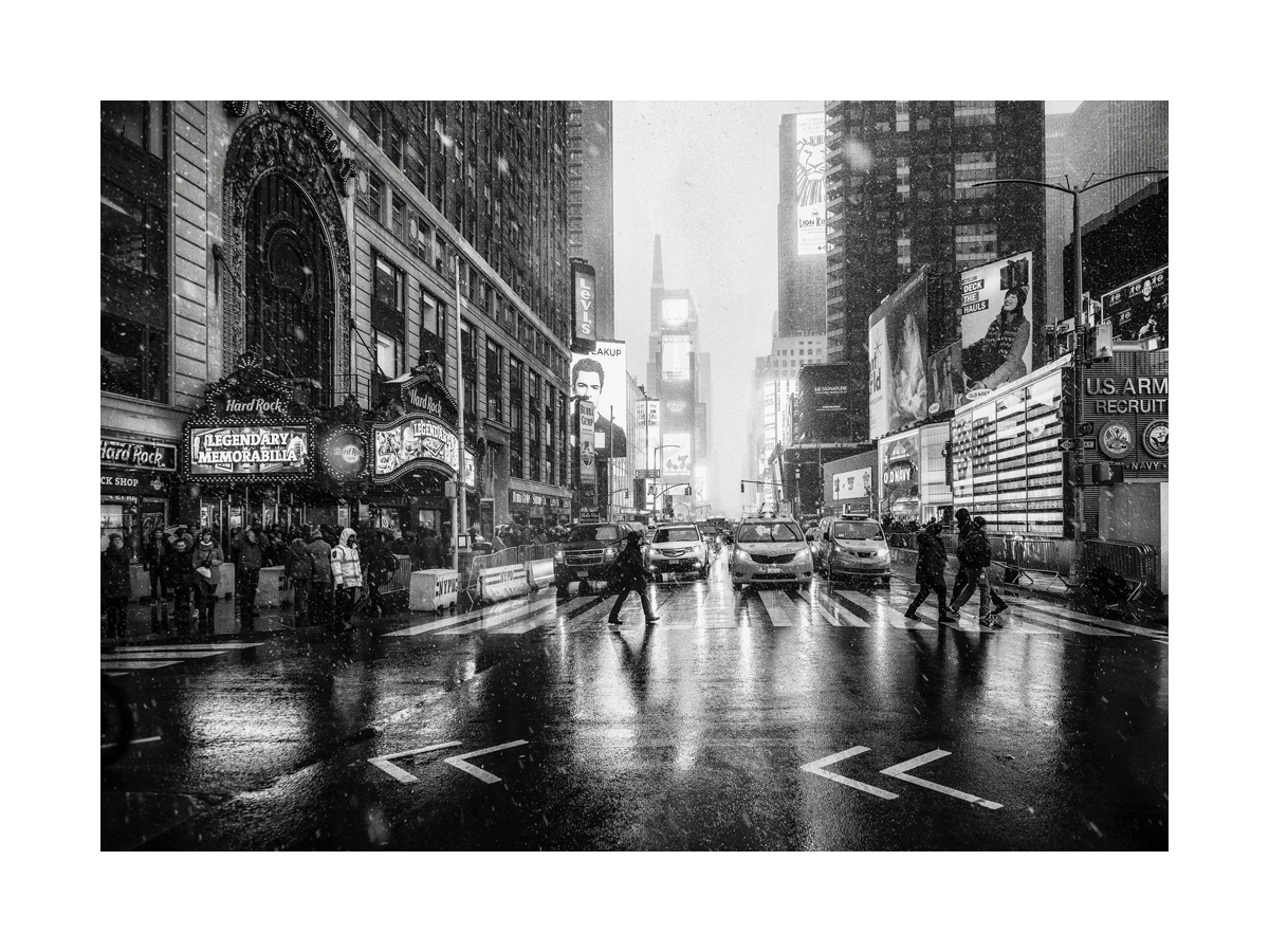 Schwarz-weiß-Fotografie des Times Square in New York während eines Schneesturms mit Autos und Menschen.