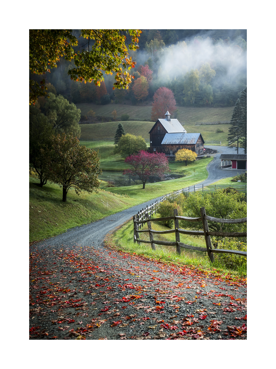 Fotografie einer Scheune auf dem Land, umgeben von bunten Herbstbäumen und Nebel.