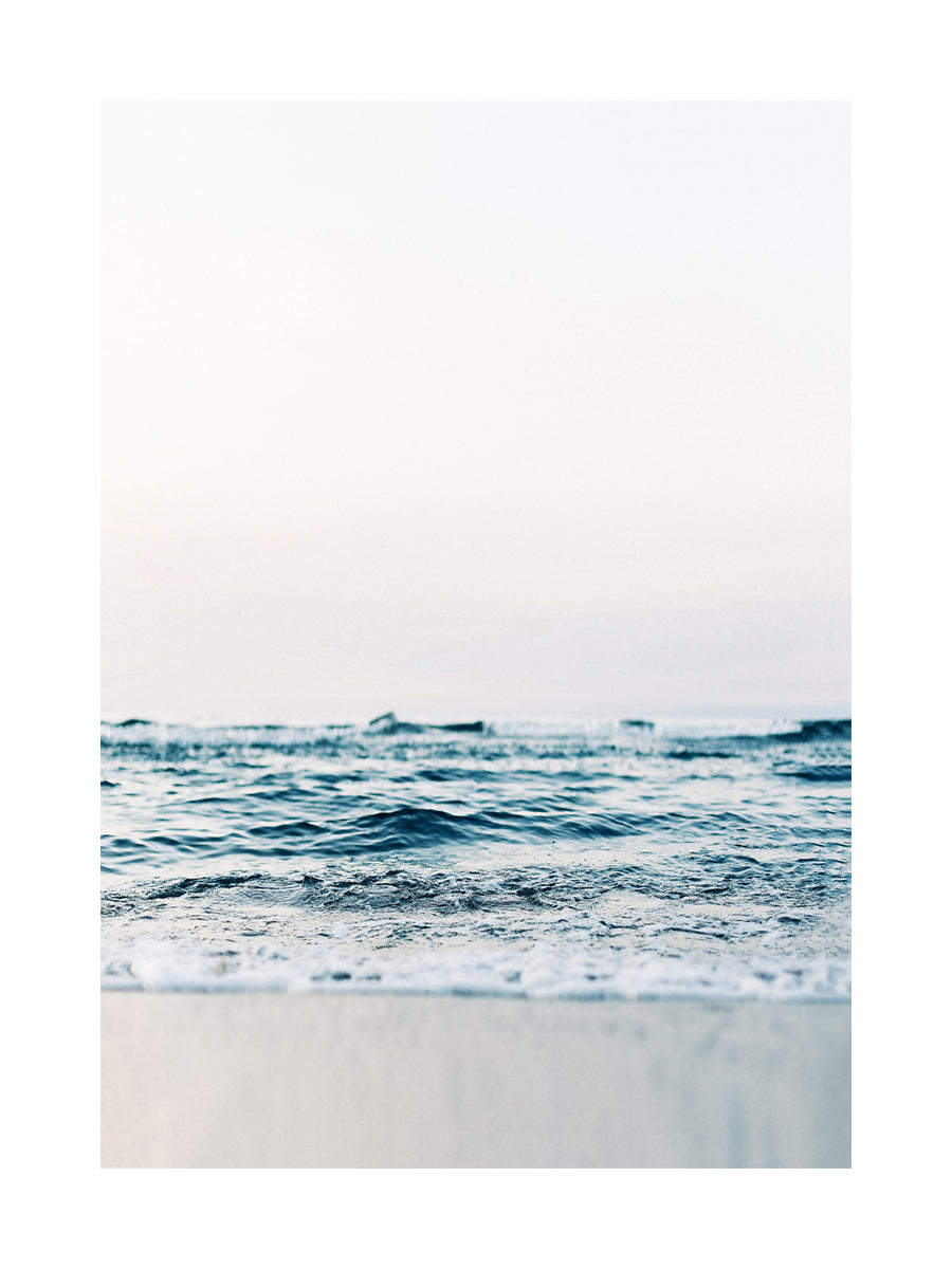 Fotografie von Wellen, die ans Ufer schlagen, mit blauem Himmel im Hintergrund.