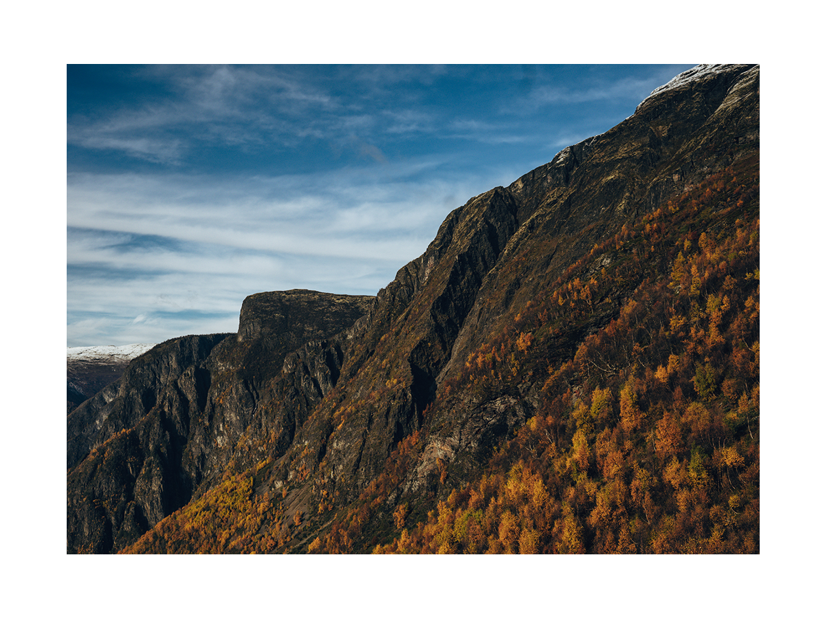 Fotografie eines Berges mit herbstlichen Bäumen und blauem Himmel.