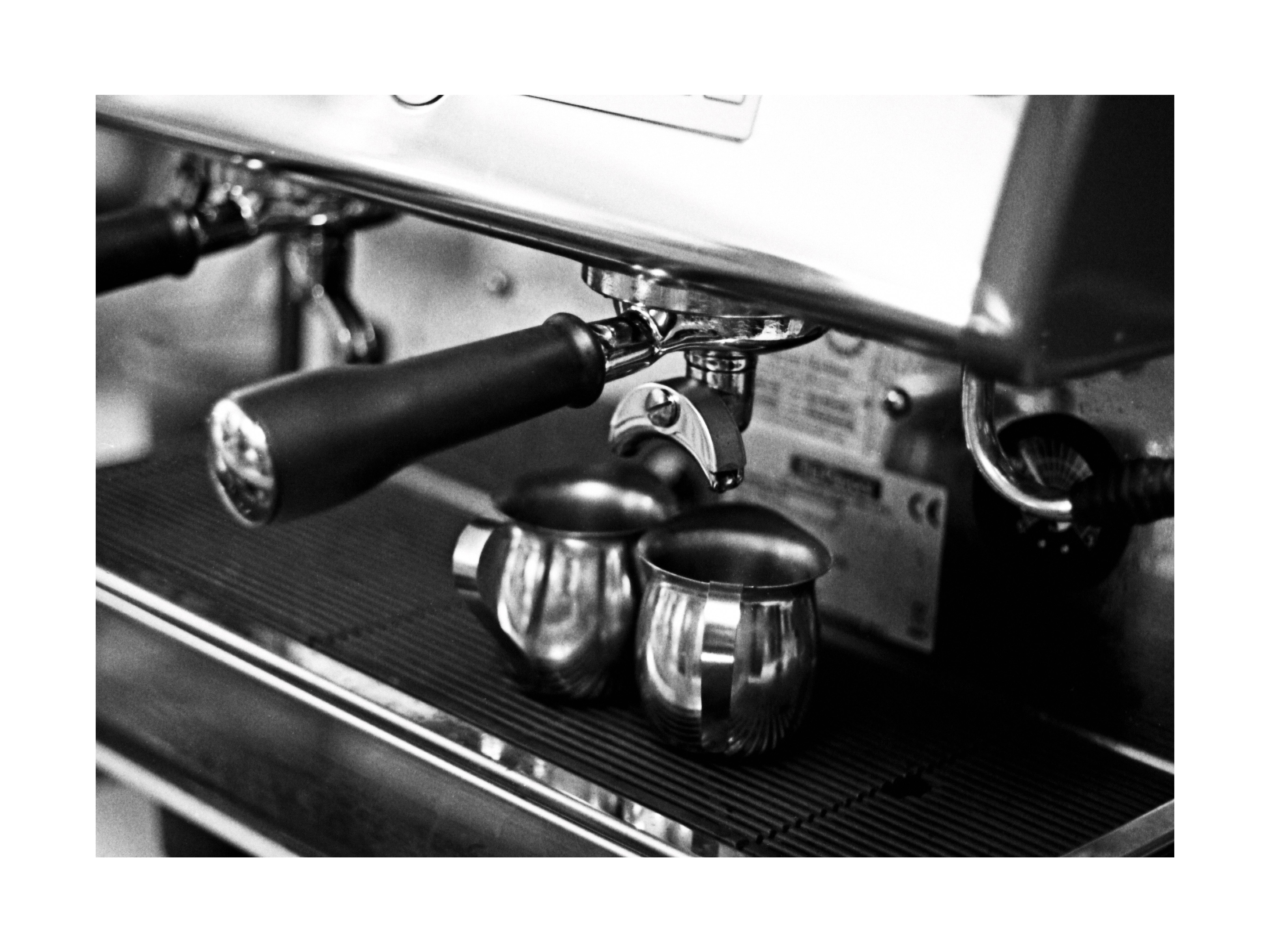 Schwarz-Weiß-Fotografie einer Espressomaschine mit zwei Metallkannen.