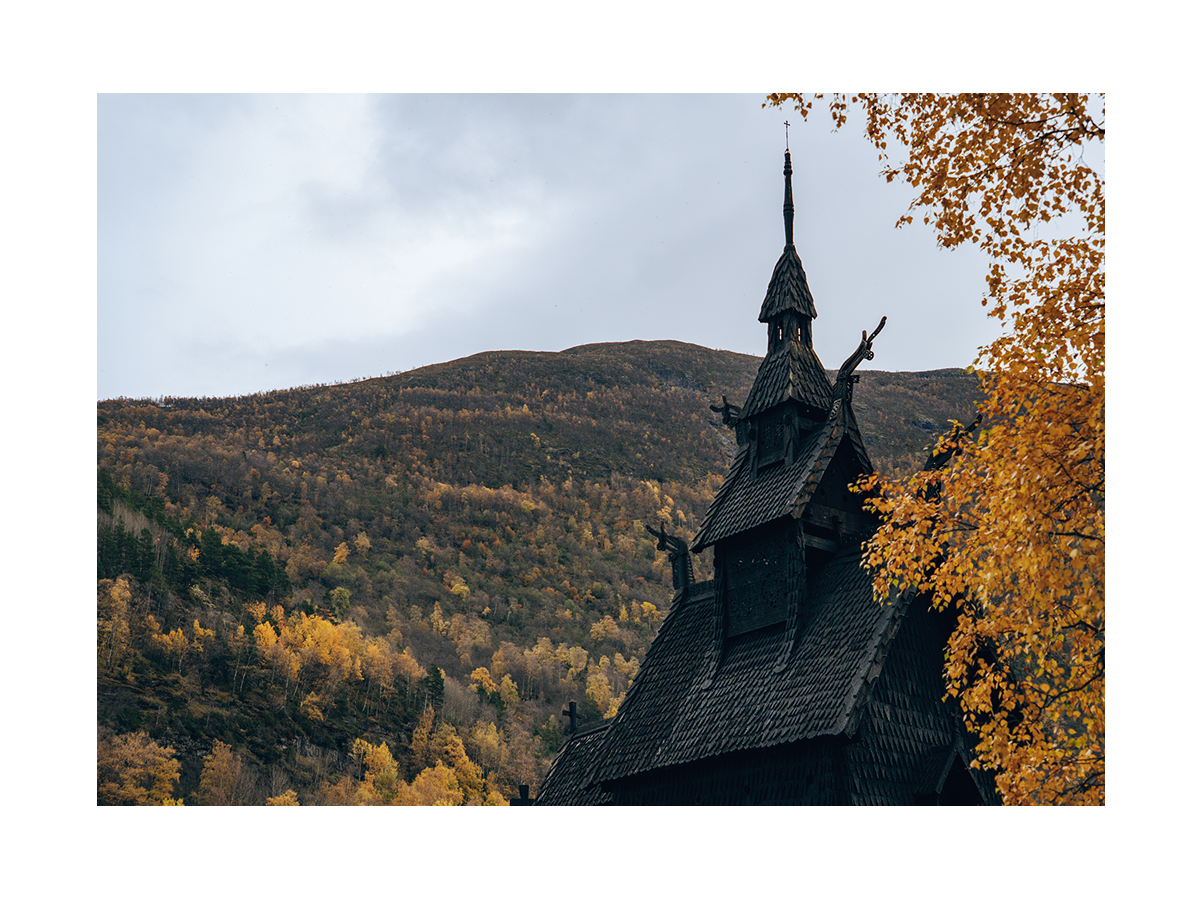 Fotografie der Borgund Stabkirche in Norwegen, umgeben von herbstlichen Bäumen und Bergen.