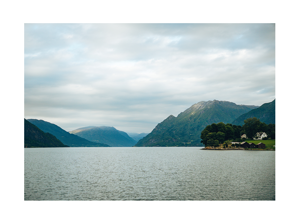 Fotografie eines Fjords mit Wasser, Bergen und einem kleinen Dorf.