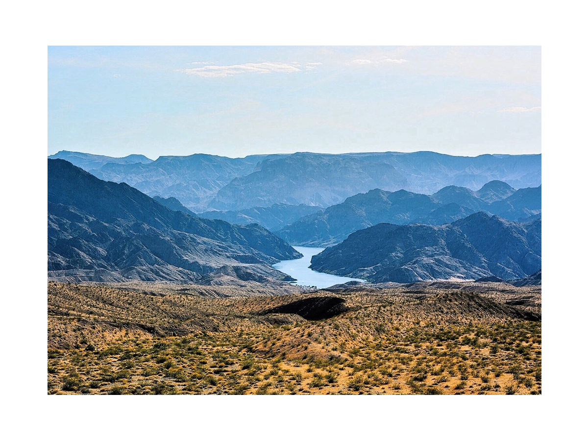Fotografie des Grand Canyon mit blauen Bergen, einem Fluss und gelbem Gras im Vordergrund.