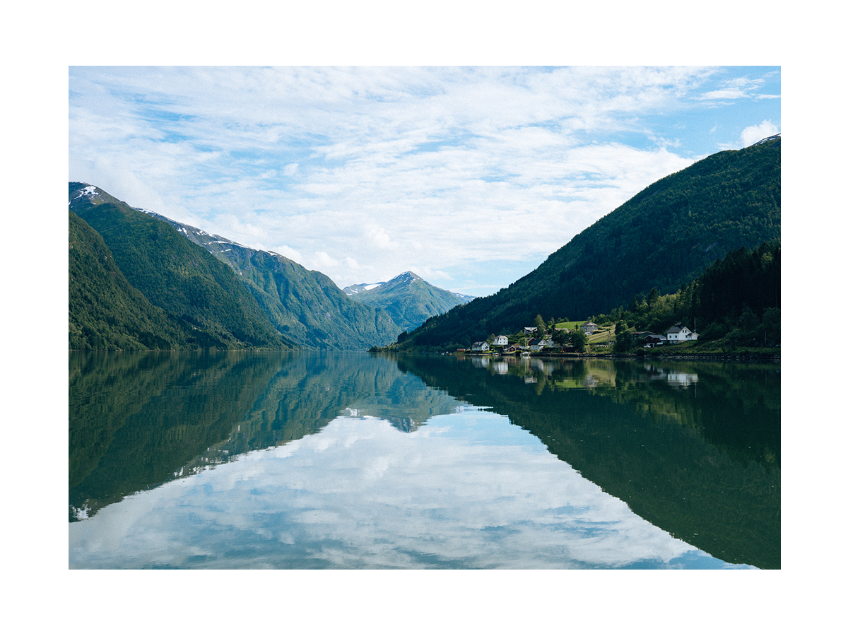 Fotografie von grünen Bergen und blauem Himmel, die sich im Wasser spiegeln.
