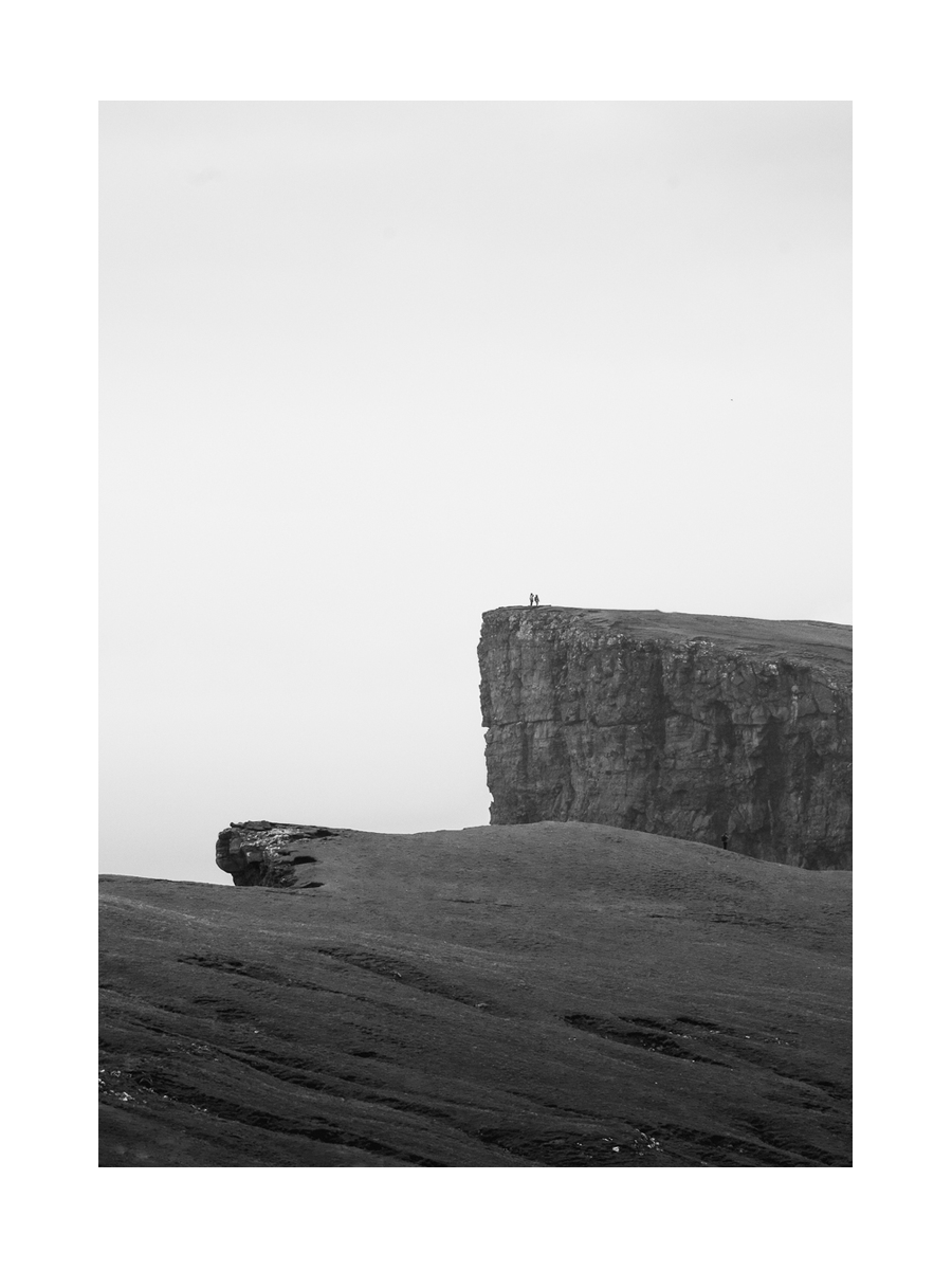 Schwarz-weiß-Fotografie von zwei Personen auf einer großen Klippe mit atemberaubender Landschaft.