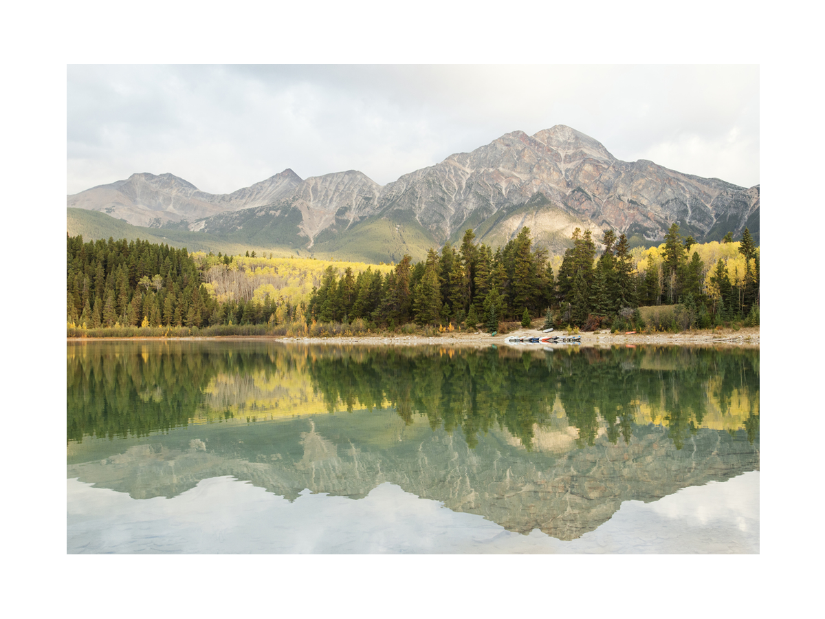 Fotografie eines Bergsees mit Wald und Bergen im Hintergrund.