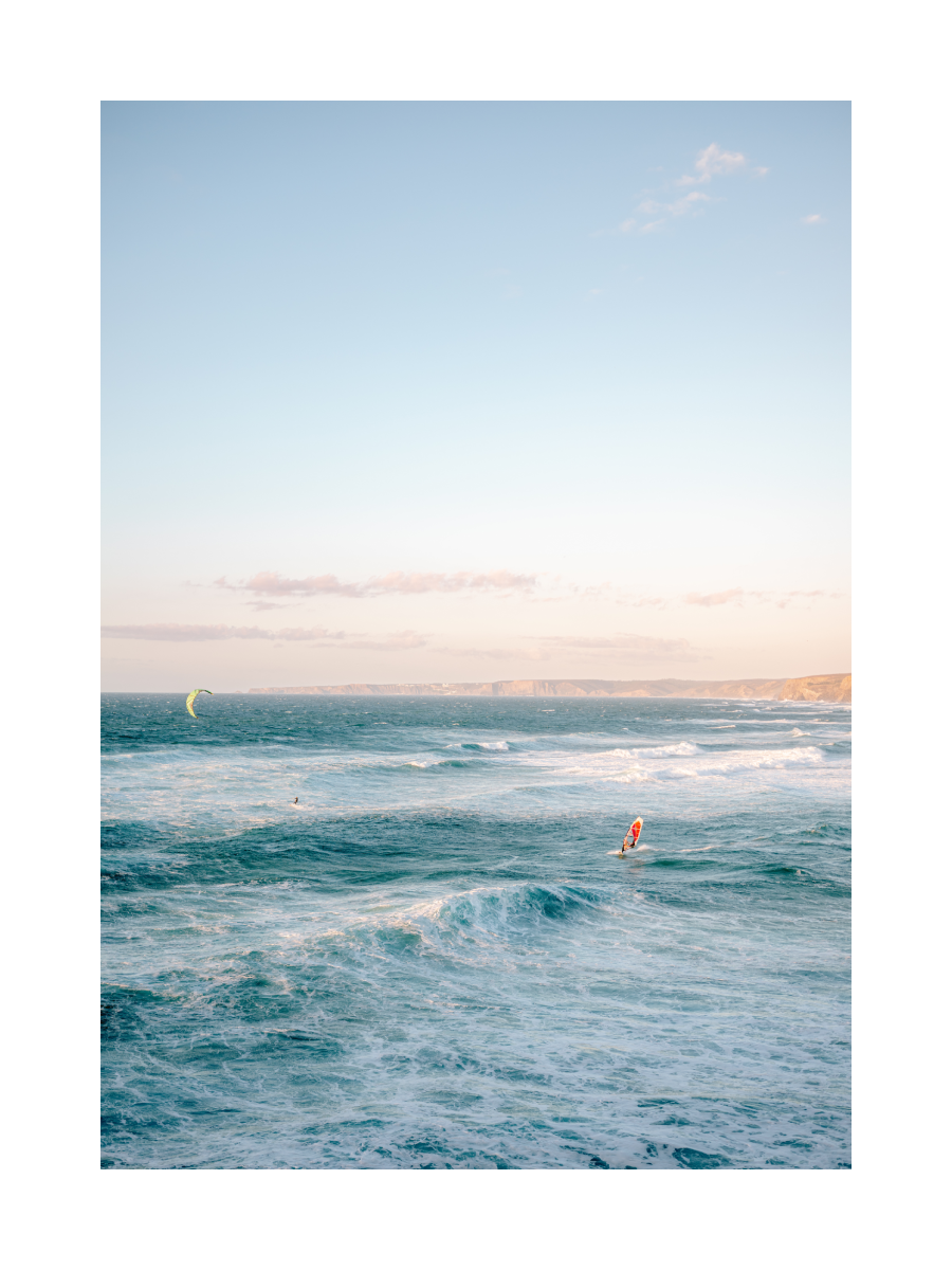 Fotoposter von Surfern auf dem Meer bei Sonnenuntergang mit Hügeln im Hintergrund.