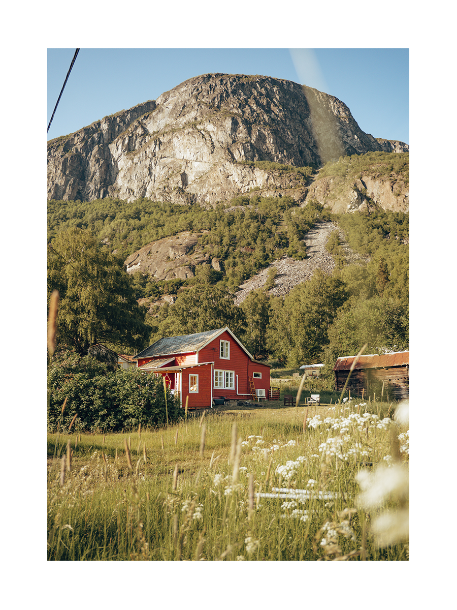Ein rotes Haus in der Natur, umgeben von grünen Bäumen und Bergen.