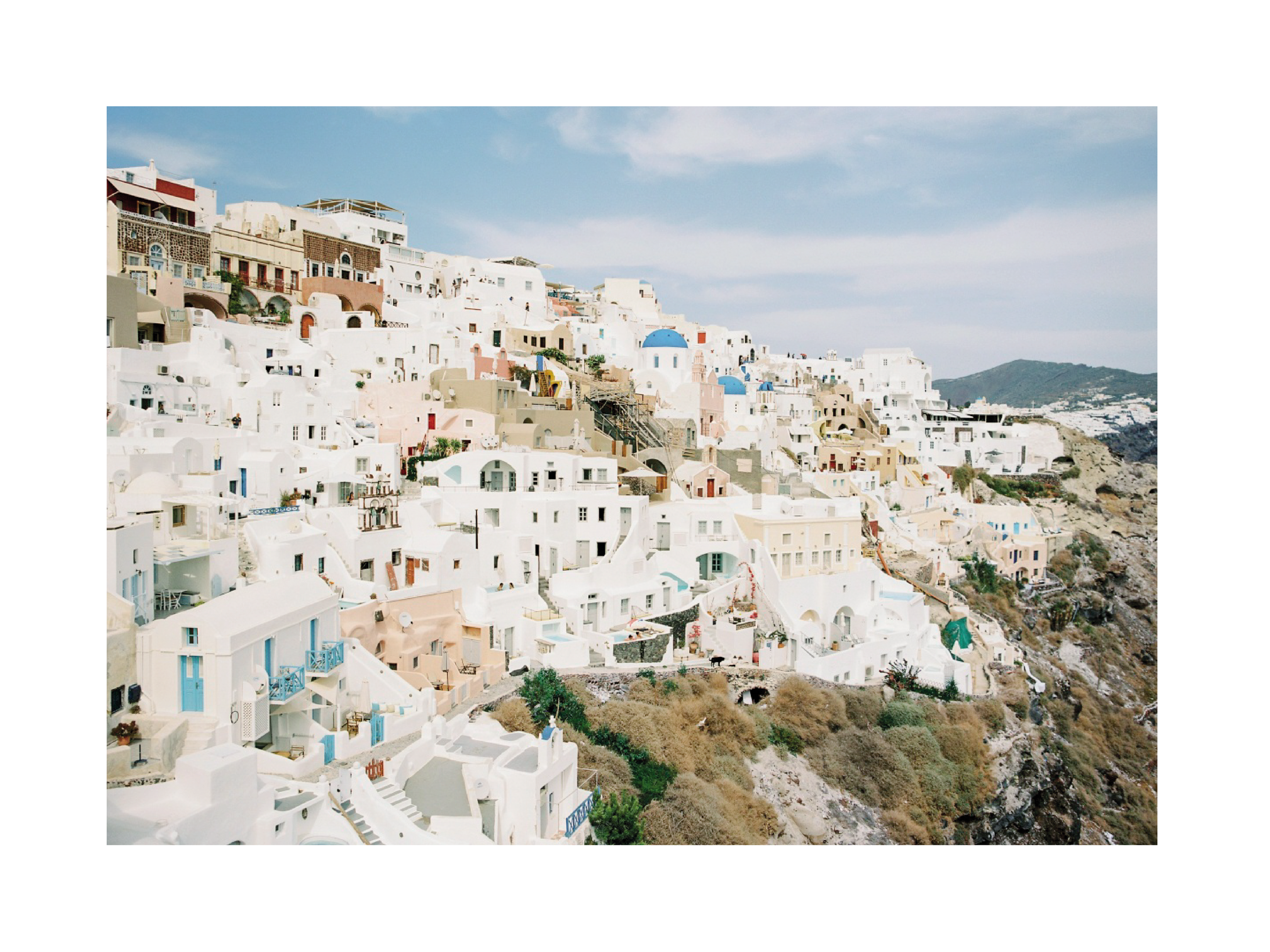 Fotografie des Dorfes Oia auf Santorini mit weiß getünchten Gebäuden und Blick auf die Ägäis.
