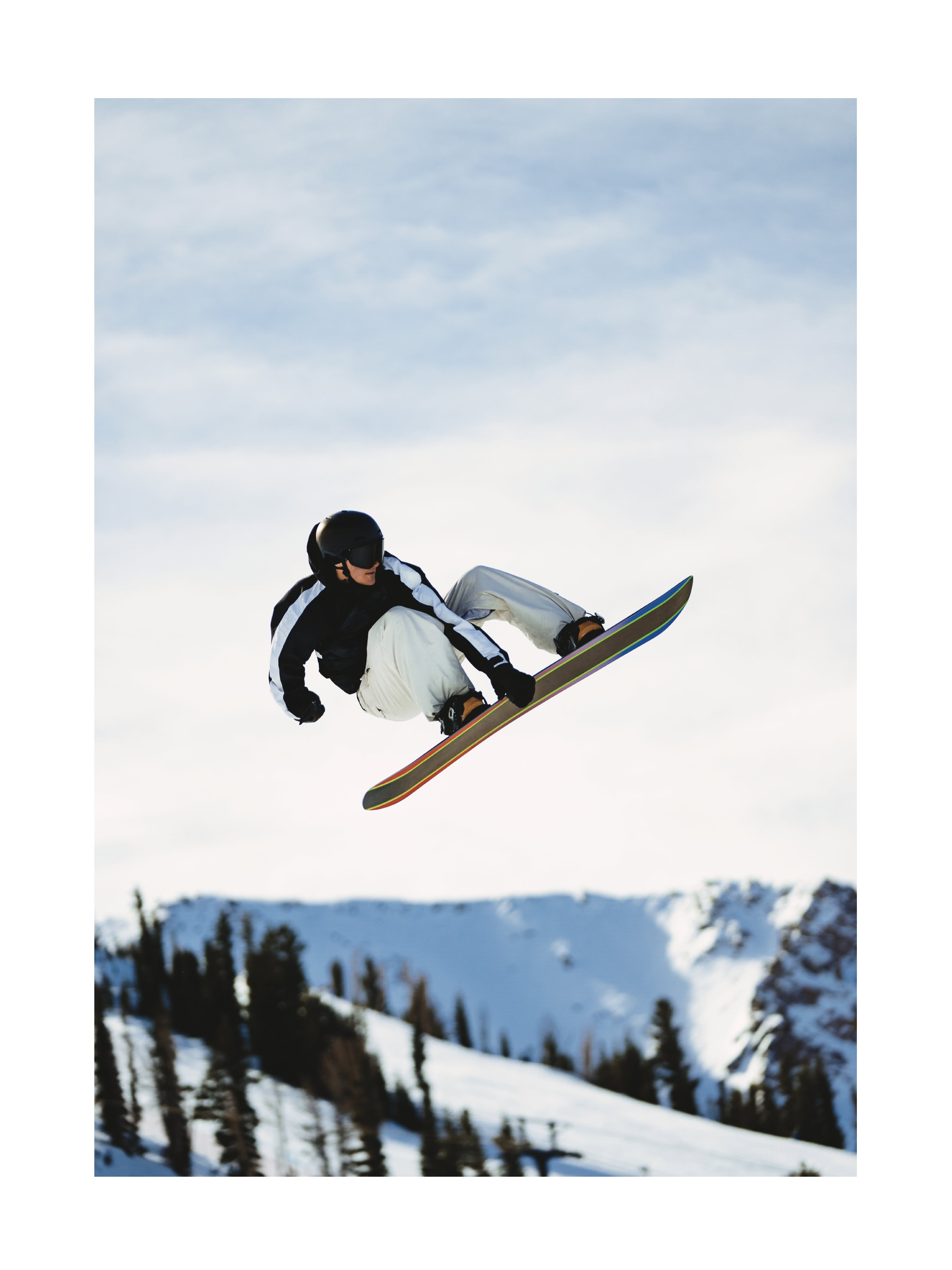 Snowboarder in der Luft vor einer verschneiten Berglandschaft.