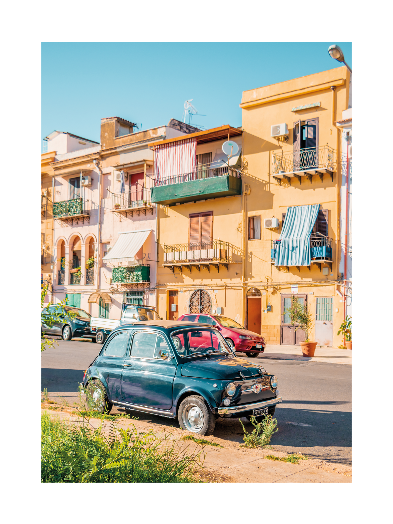 Straßenszene in Sizilien mit einem klassischen Fiat 500 vor bunten Gebäuden.