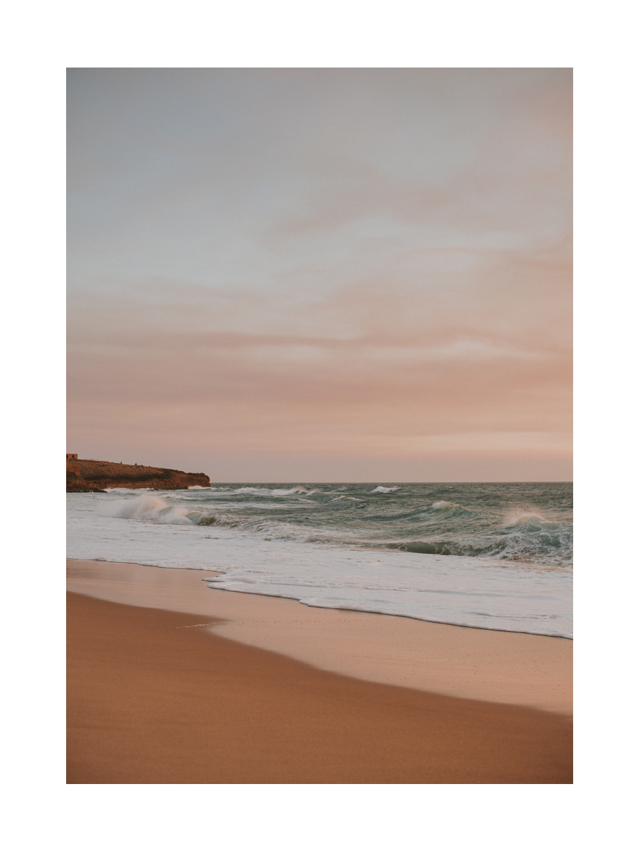 Fotografie eines Sandstrandes bei Sonnenuntergang mit sanften Wellen und pastellfarbenem Himmel.