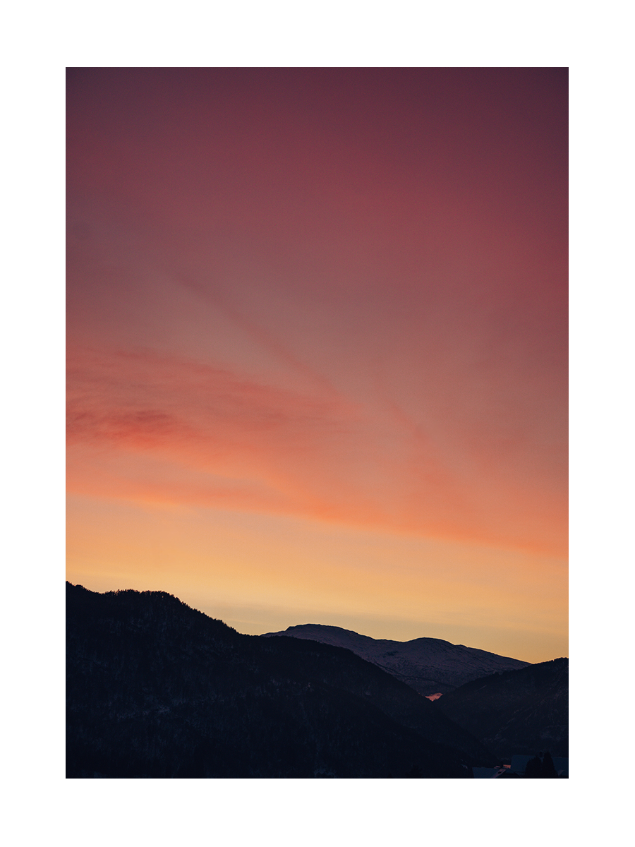 Sonnenuntergang über einer Berglandschaft mit orangefarbenem und violettem Himmel.