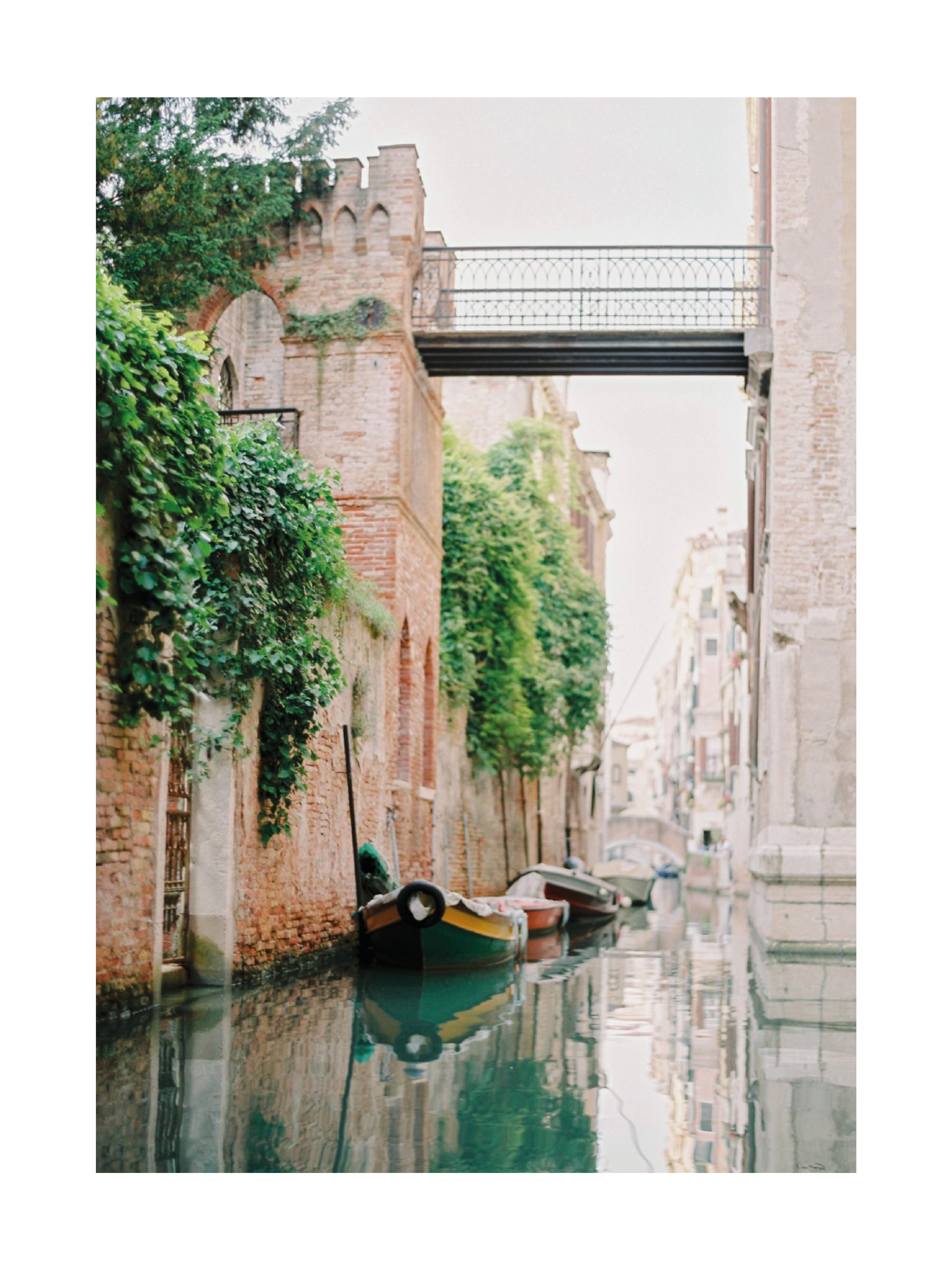 Fotografie von Booten an einem Kai in einem venezianischen Kanal mit einem von Pflanzen bedeckten Gebäude.