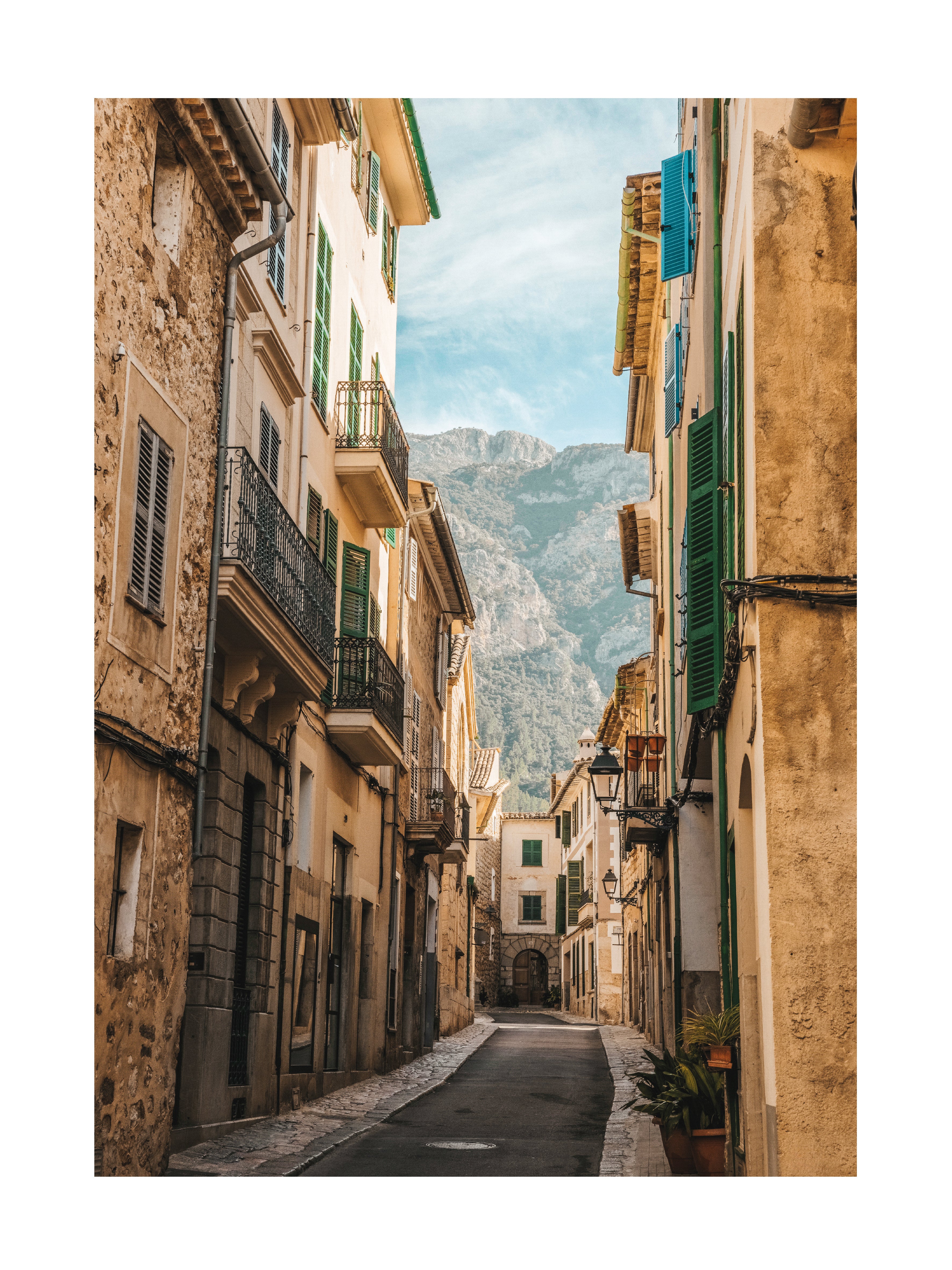Fotografie einer Straße auf Mallorca mit alten Gebäuden und einem Berg im Hintergrund.
