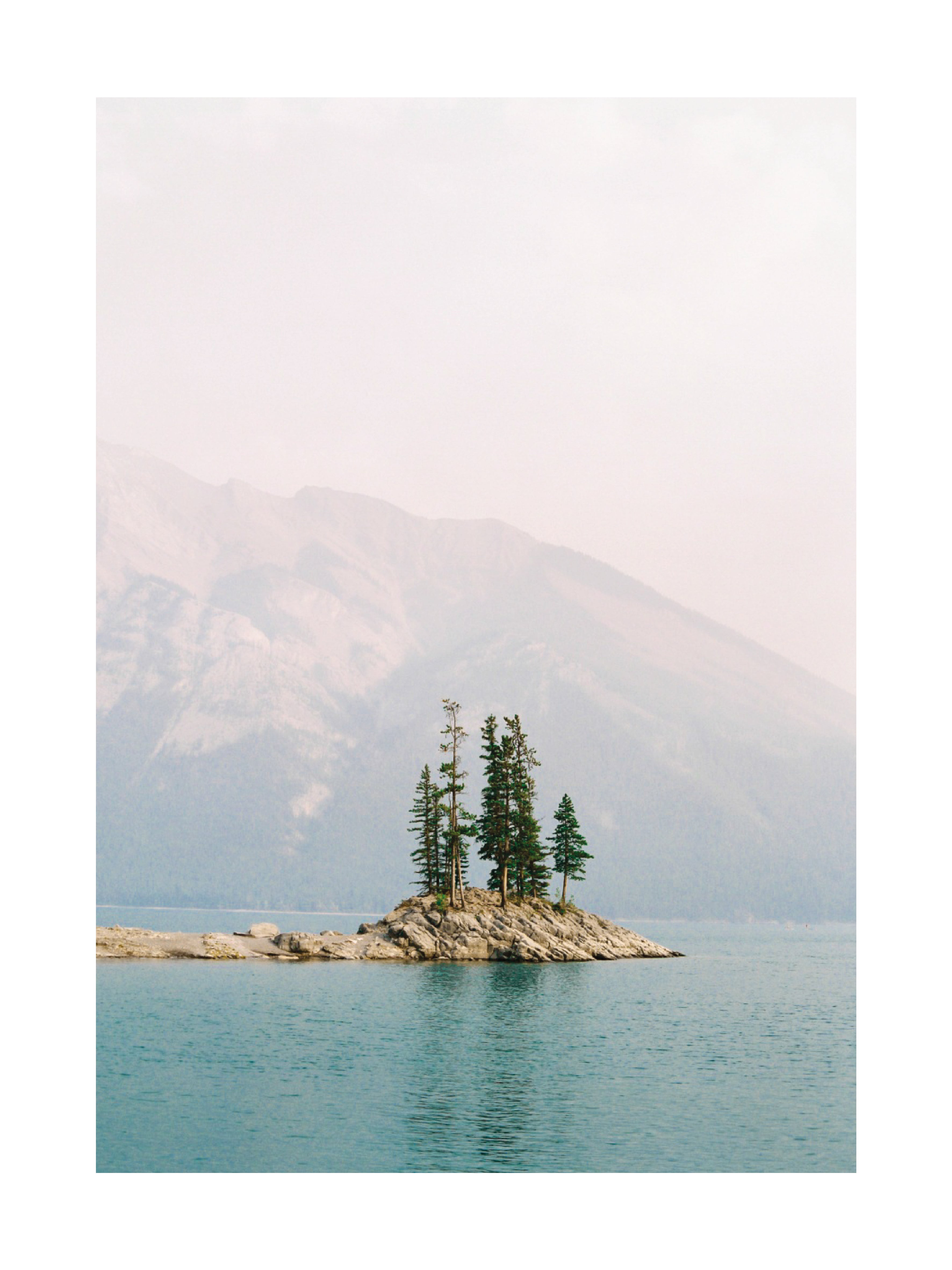 Fotografie von Lake Minnewanka mit einer kleinen Insel und Bergen im Hintergrund.