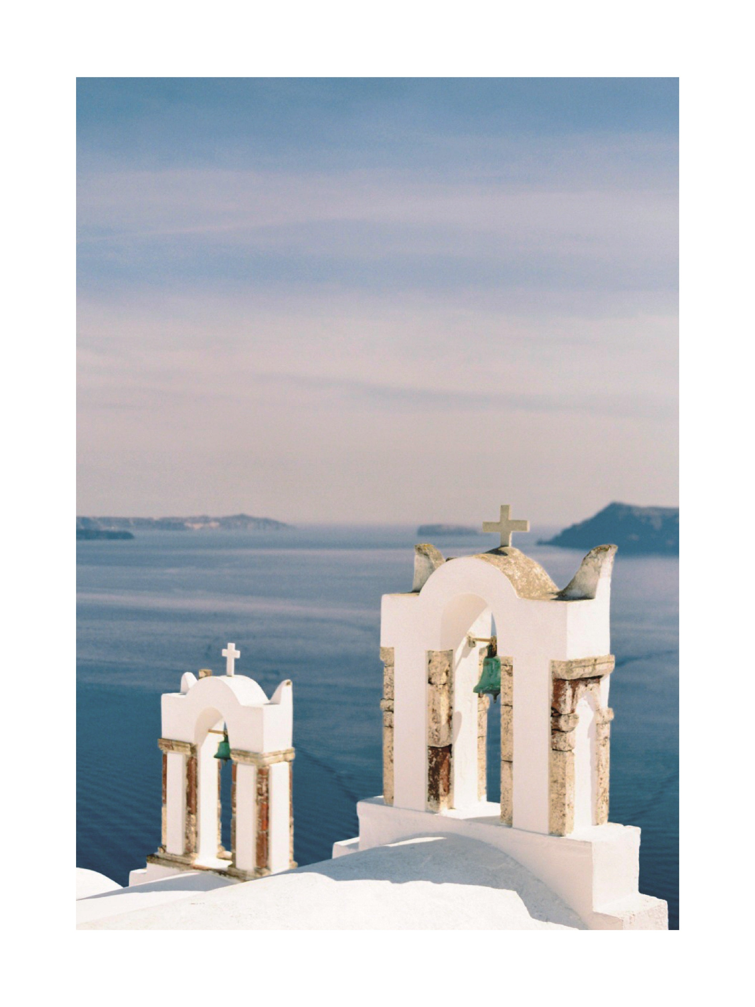 Zwei Kirchenglocken mit goldenen Kreuzen vor einem blauen Meer und klarem Himmel.