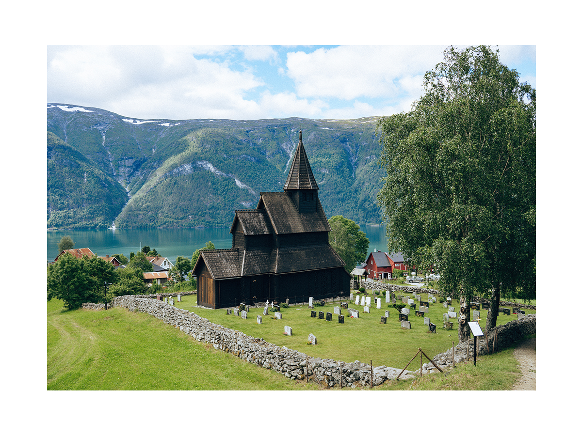 Fotografie der Stabkirche von Urnes in Norwegen mit umliegenden Bergen und Fjord.
