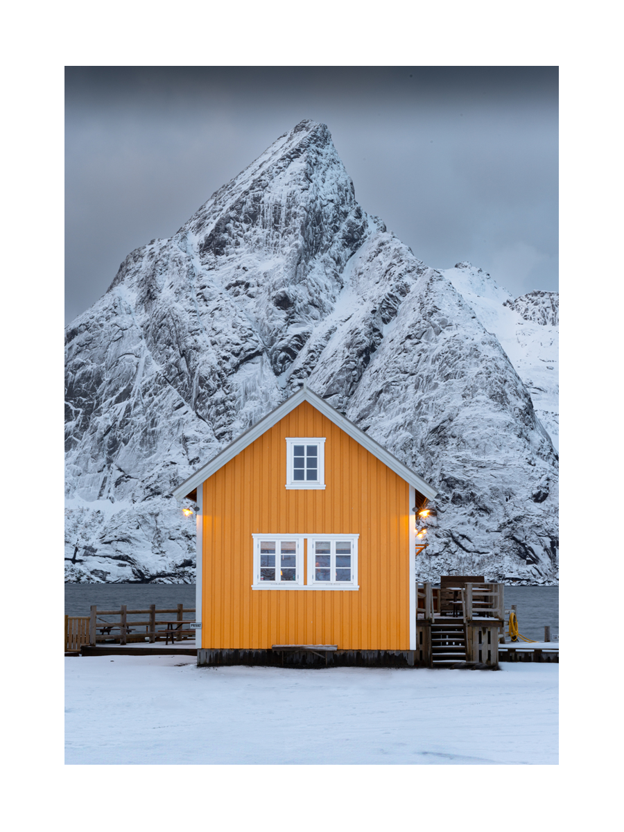 Ein gelbes Haus vor einer schneebedeckten Berglandschaft.