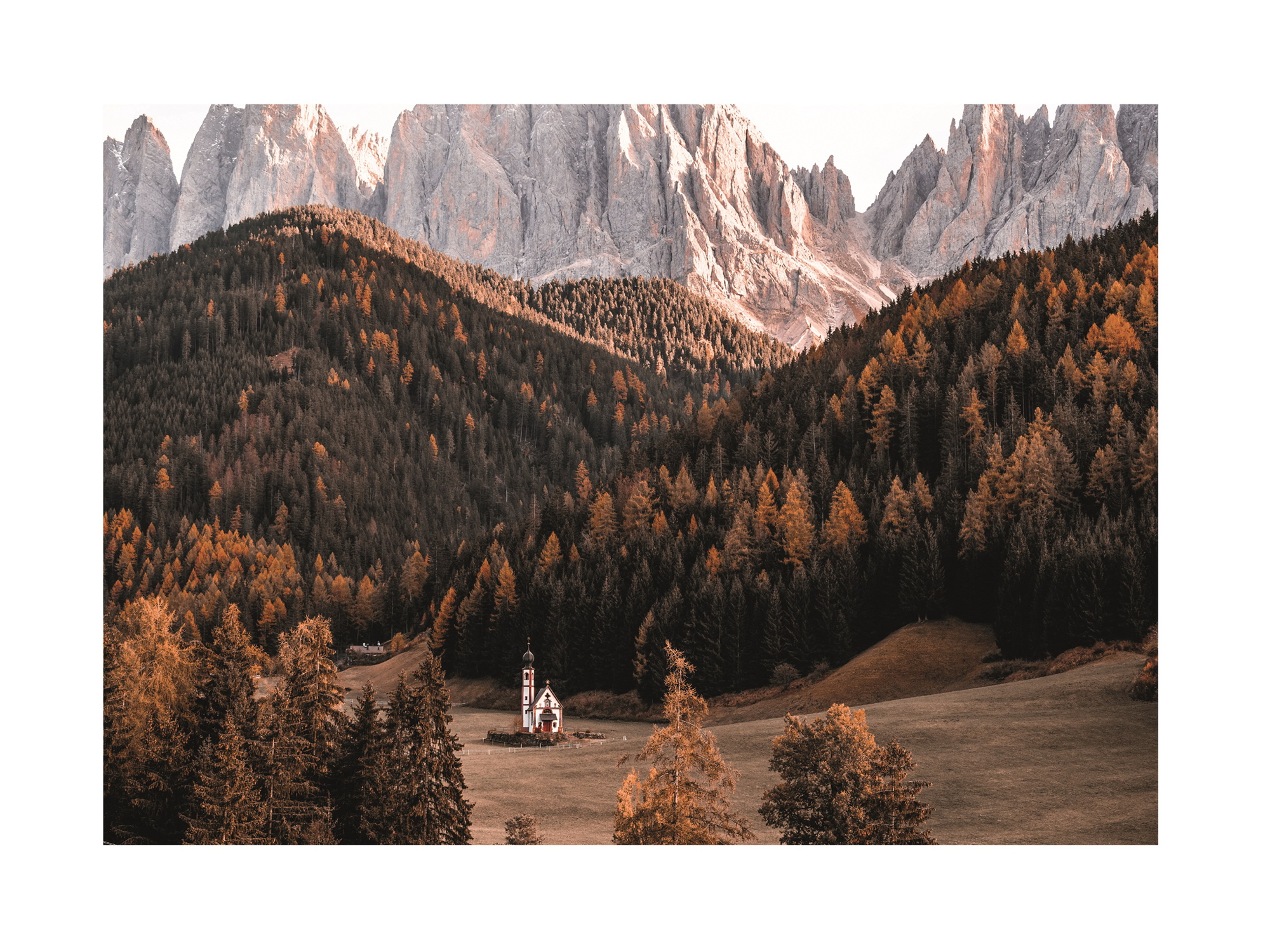 Fotografie einer Kirche in herbstlicher Landschaft mit Bergen im Hintergrund.
