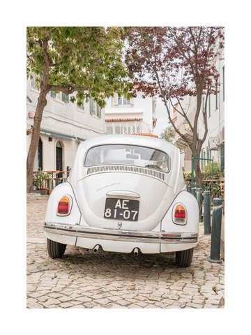Fotografie eines weißen Oldtimers auf einer gepflasterten Dorfstraße.