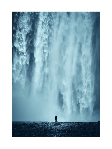 Fotografie eines großen Wasserfalls mit einer Person, die auf einem Felsen steht.