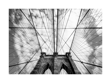 Schwarz-weiß-Fotografie der Brooklyn Bridge von unten mit Wolken am Himmel.