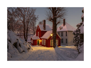 Ein rotes Haus in einer verschneiten Landschaft bei Nacht mit beleuchteter Straßenlaterne.