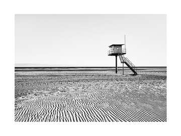 Schwarz-weiß Fotografie eines verlassenen Rettungsturms an einem leeren Strand.