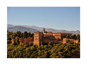 Fotografie der Alhambra in Granada mit blauem Himmel und Bergen im Hintergrund.