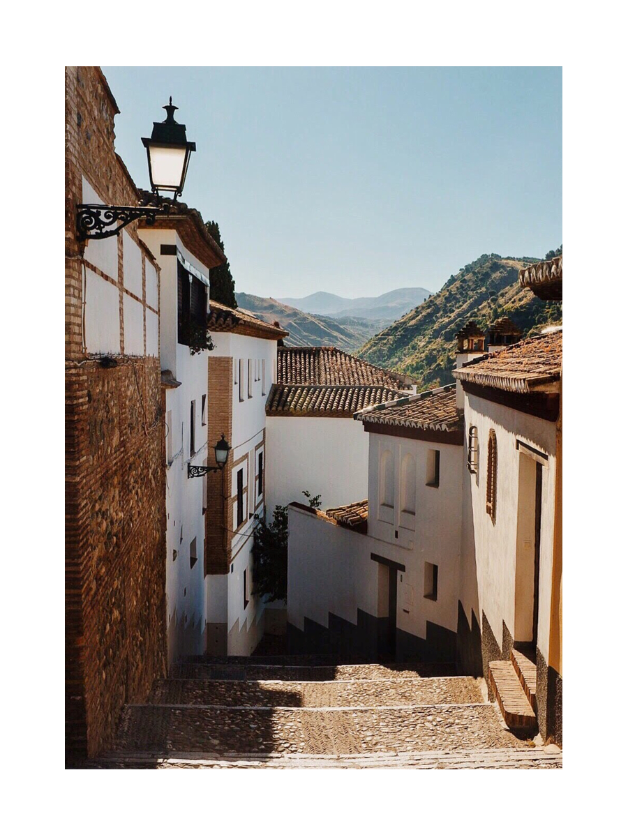 Eine Gasse in der Altstadt von Granada mit weißen Häusern und Blick auf die Berge.