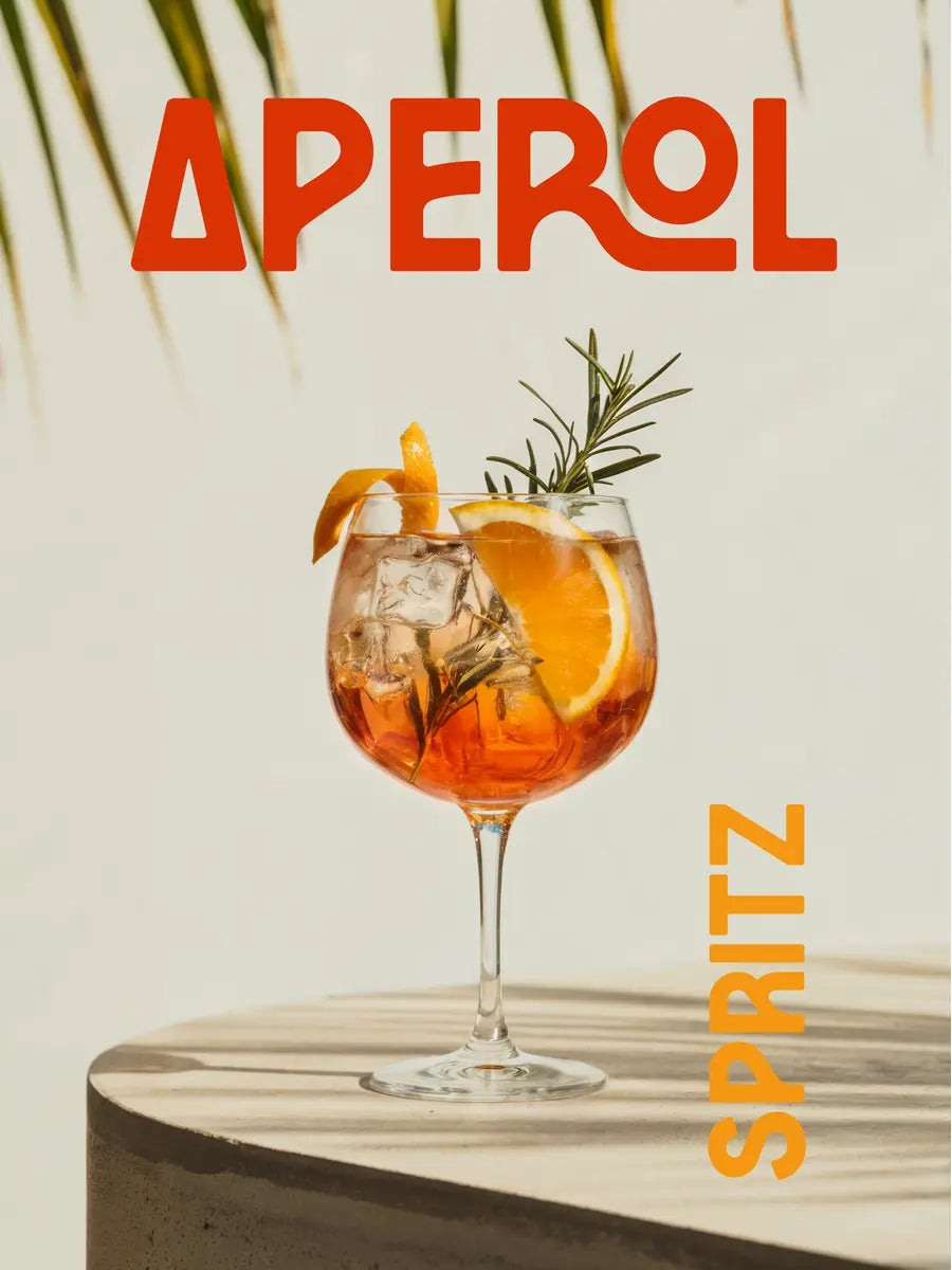Ein Aperol Spritz in einem Glas mit Orangenscheiben und Rosmarinzweig, umgeben von Palmen und orangefarbener Schrift.