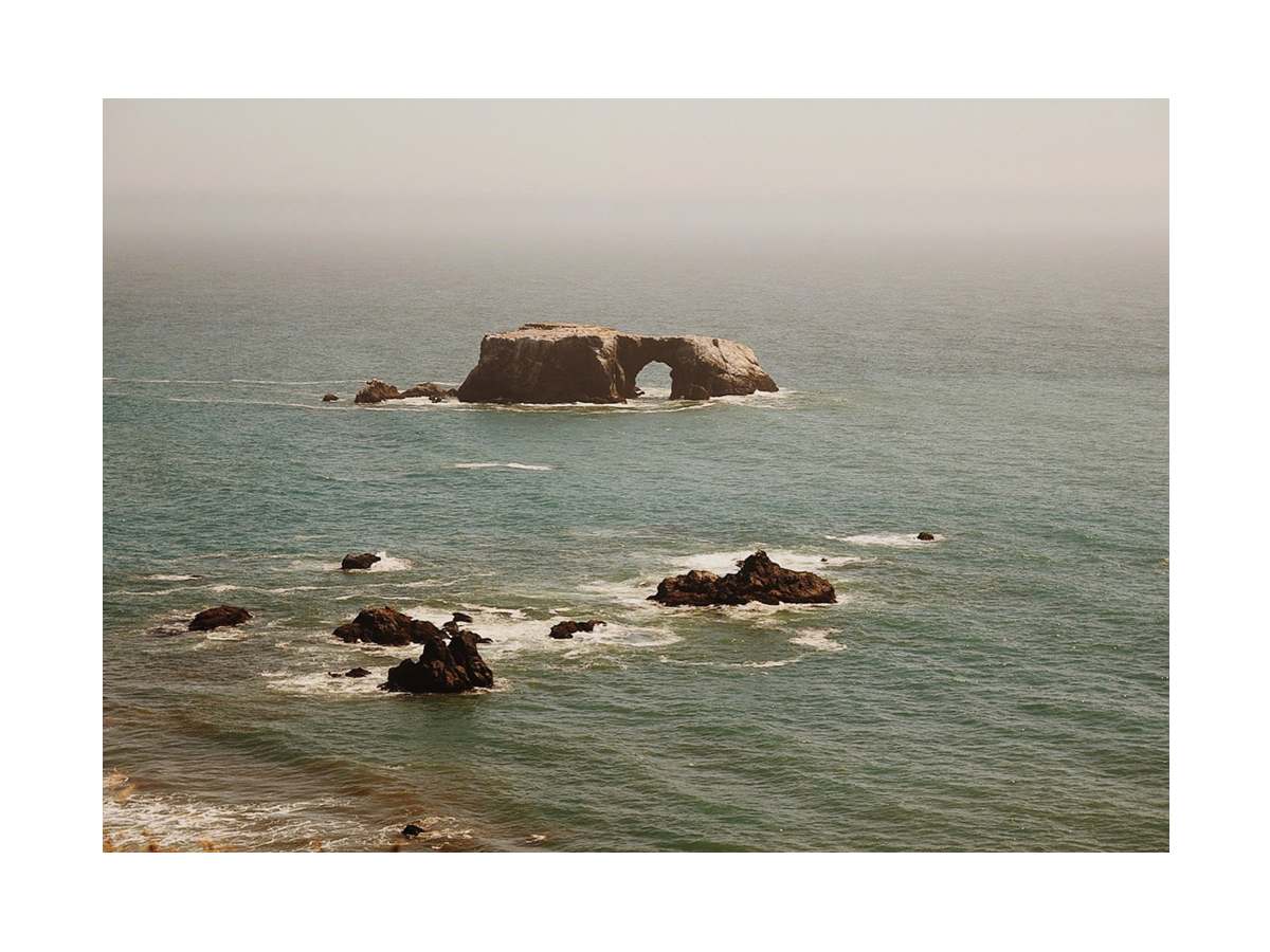 Fotografie eines Felsbogens im Meer mit kleineren Felsen in der Umgebung.