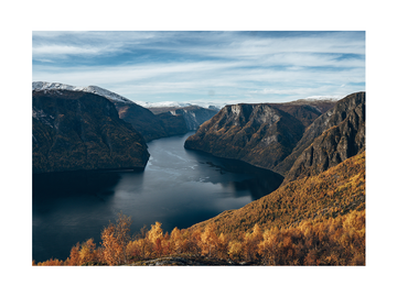 Fotografie eines Fjords mit schneebedeckten Bergen und herbstlichen Bäumen.