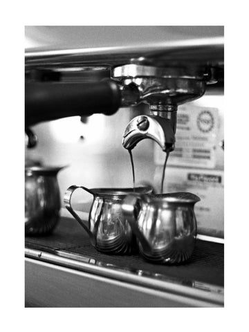 Schwarz-Weiß-Fotografie einer Espressomaschine, die Espresso in zwei Metallkännchen gießt.