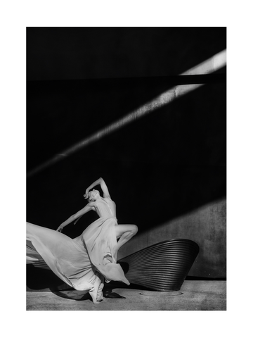 Schwarzweiß-Fotografie einer Ballerina in einem weißen Kleid, die auf einem schwarzen Stuhl tanzt.
