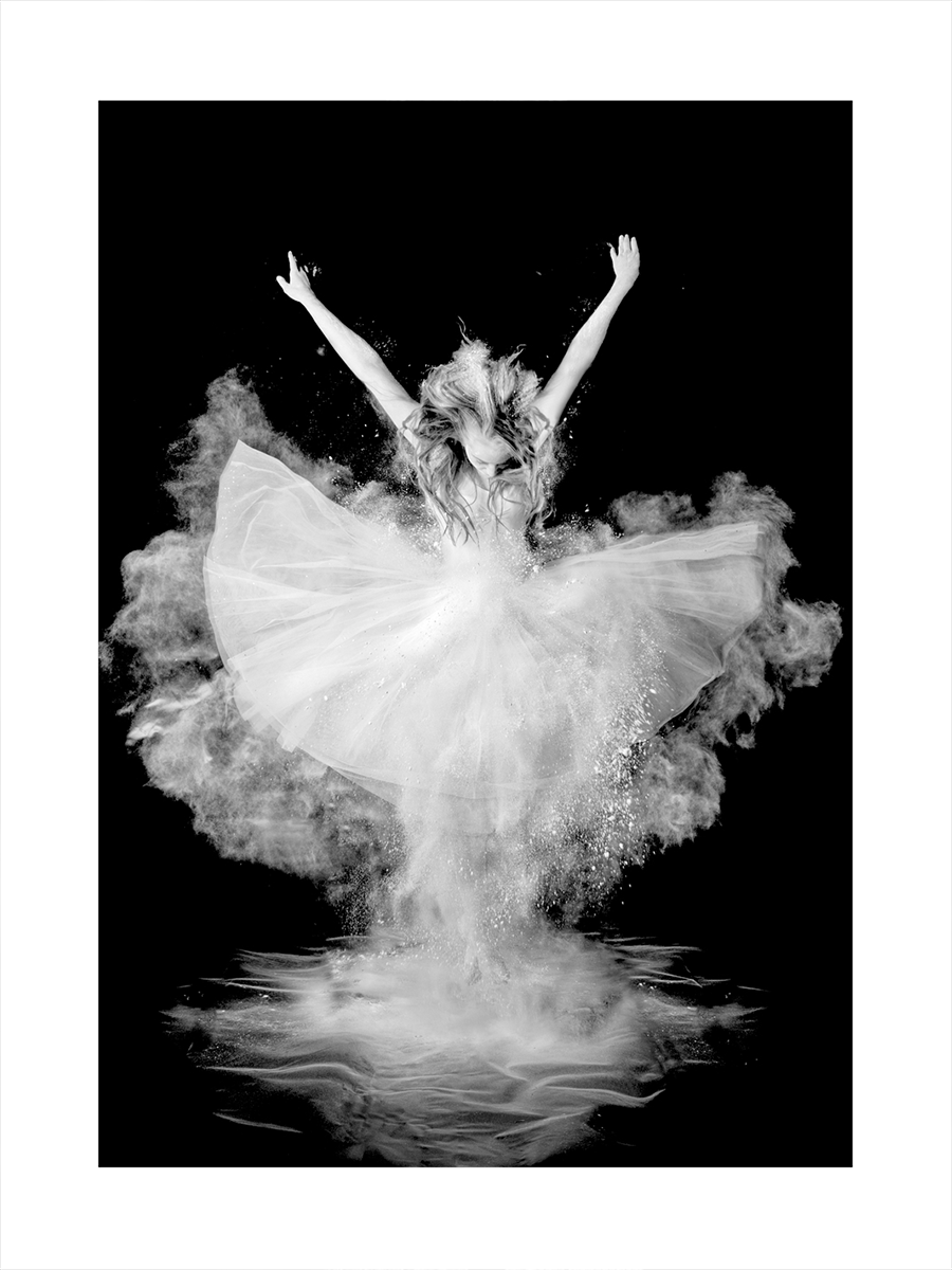 Schwarz-weiß-Fotografie einer Balletttänzerin in einem weißen Kleid mit Puder vor schwarzem Hintergrund.