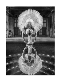 Schwarz-weiß-Fotografie einer Ballerina, die sich auf der Bühne nach vorne beugt und sich im Boden spiegelt.