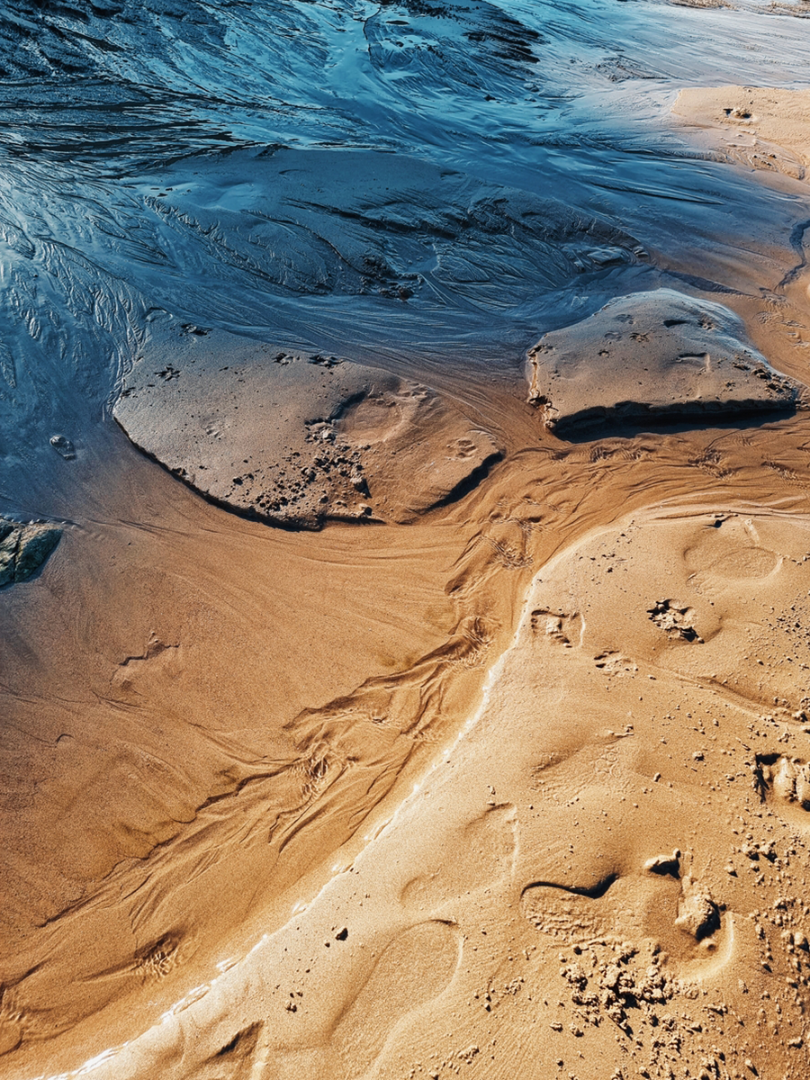 Luftaufnahme eines Strandes mit Wasser, das über den Sand fließt.