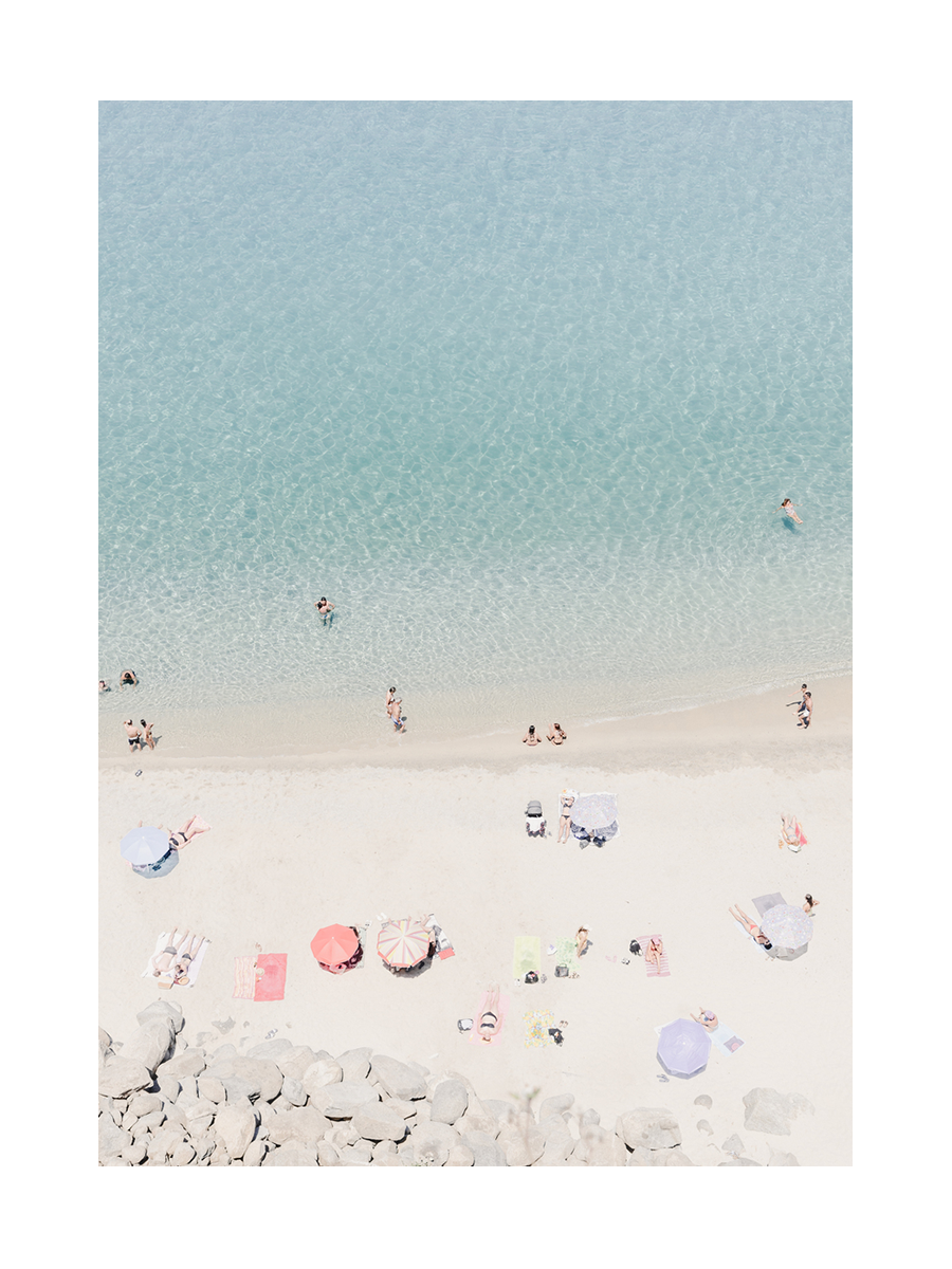Luftaufnahme eines Strandes mit Menschen im Wasser und auf bunten Handtüchern unter Sonnenschirmen.