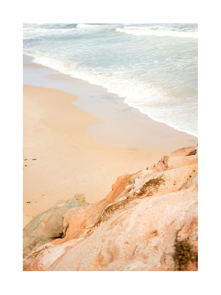 Fotografie eines Strandes mit Wellen und rosa Klippen im Vordergrund.